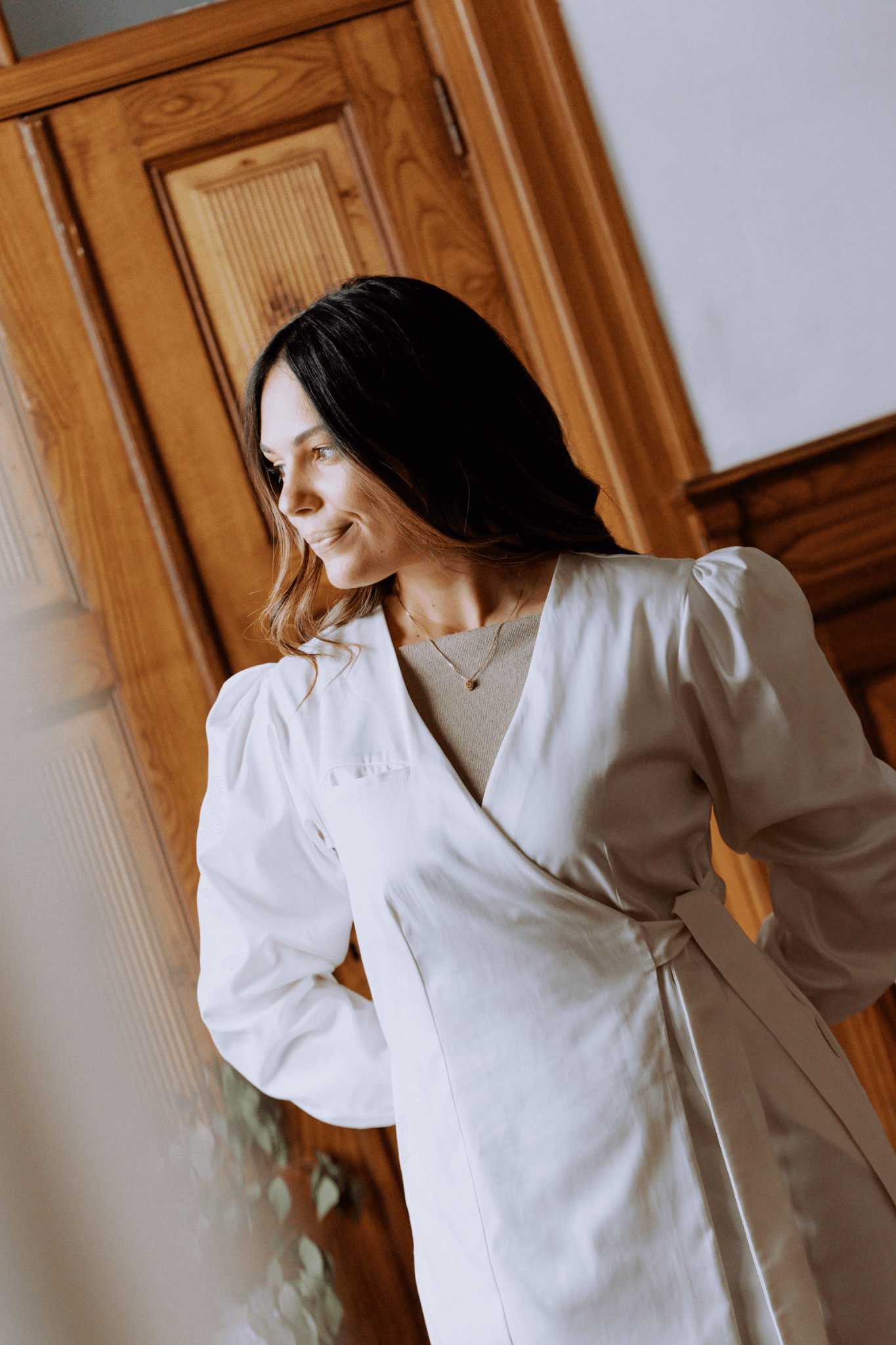 Mulher elegante usando bata Agnodice com mangas volumosas em ambiente acolhedor.