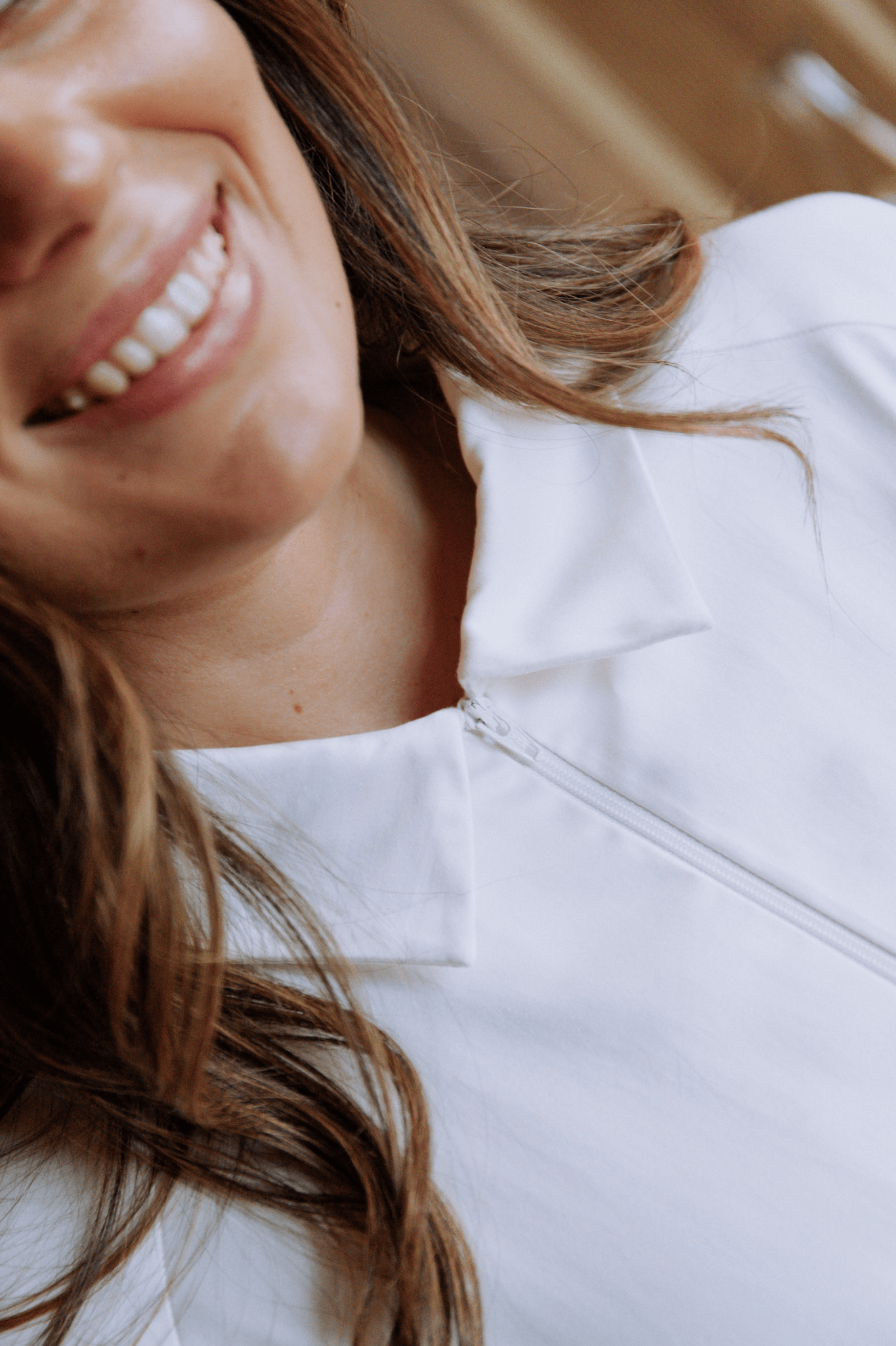 Mulher sorrindo usando uma bata branca com gola estruturada, destacando elegância e design minimalista.