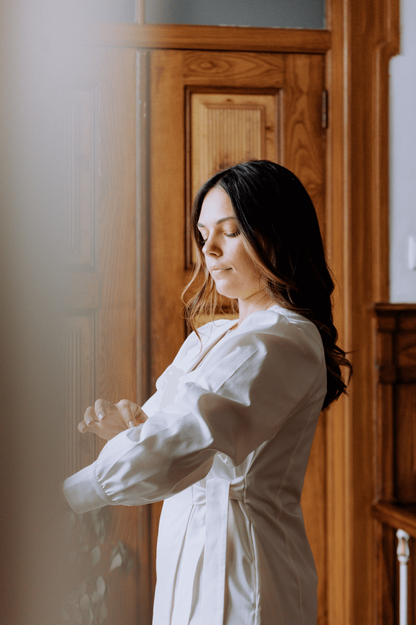 Mulher ajustando o punho de sua bata Agnodice, em primeiro plano, em um ambiente rústico e elegante.