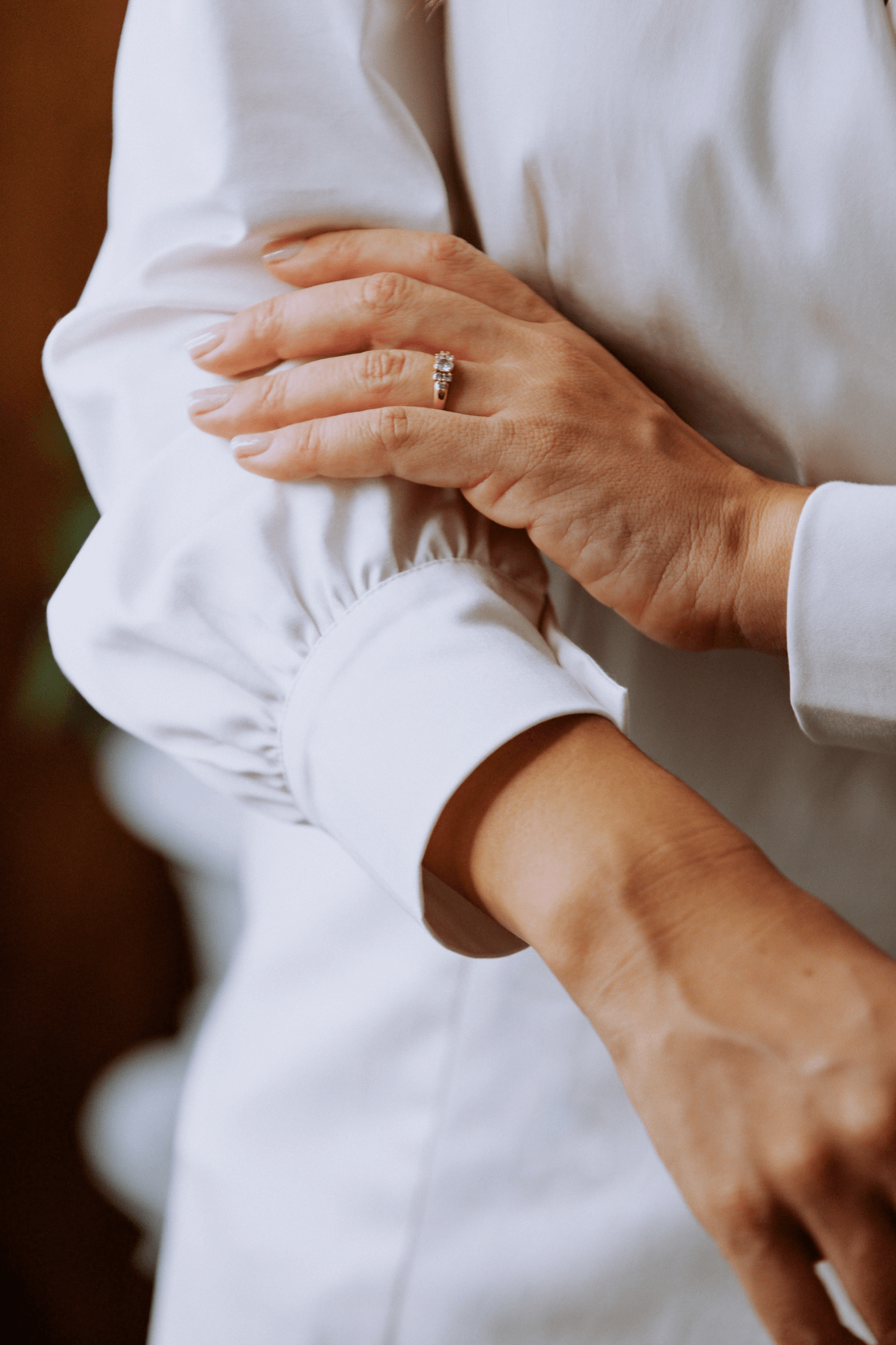 Close-up of a woman's hand adjusting the cuff of a white blouse, showcasing elegant design details.