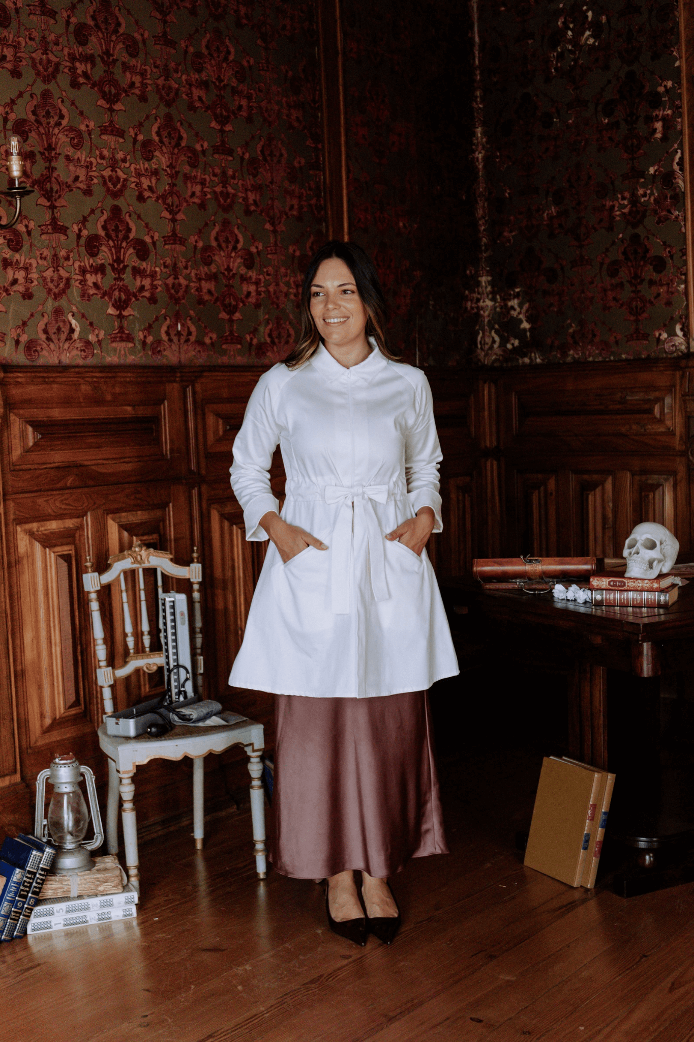 Mulher vestindo bata branca com cinto, elegante e minimalista, em ambiente clássico e acolhedor.