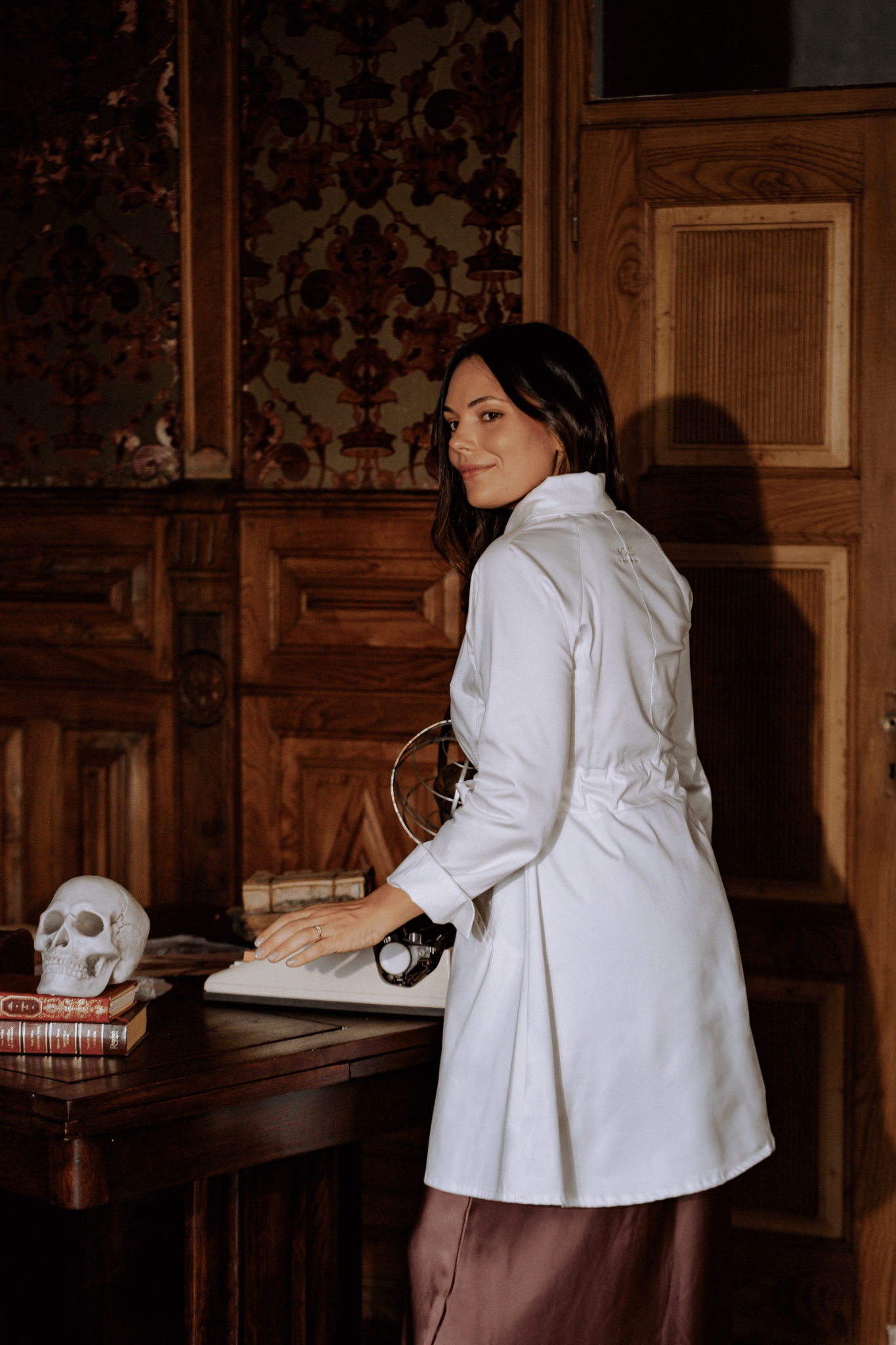 Woman wearing a white lab coat, showcasing elegance and functionality in a vintage study setting.