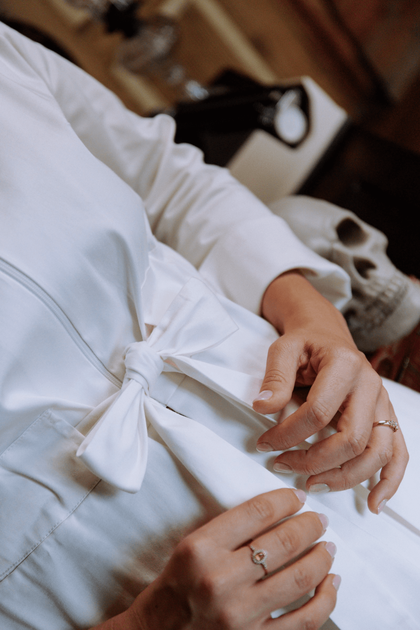 Close-up of hands adjusting the bow of a white lab coat, highlighting elegance and functionality in design.